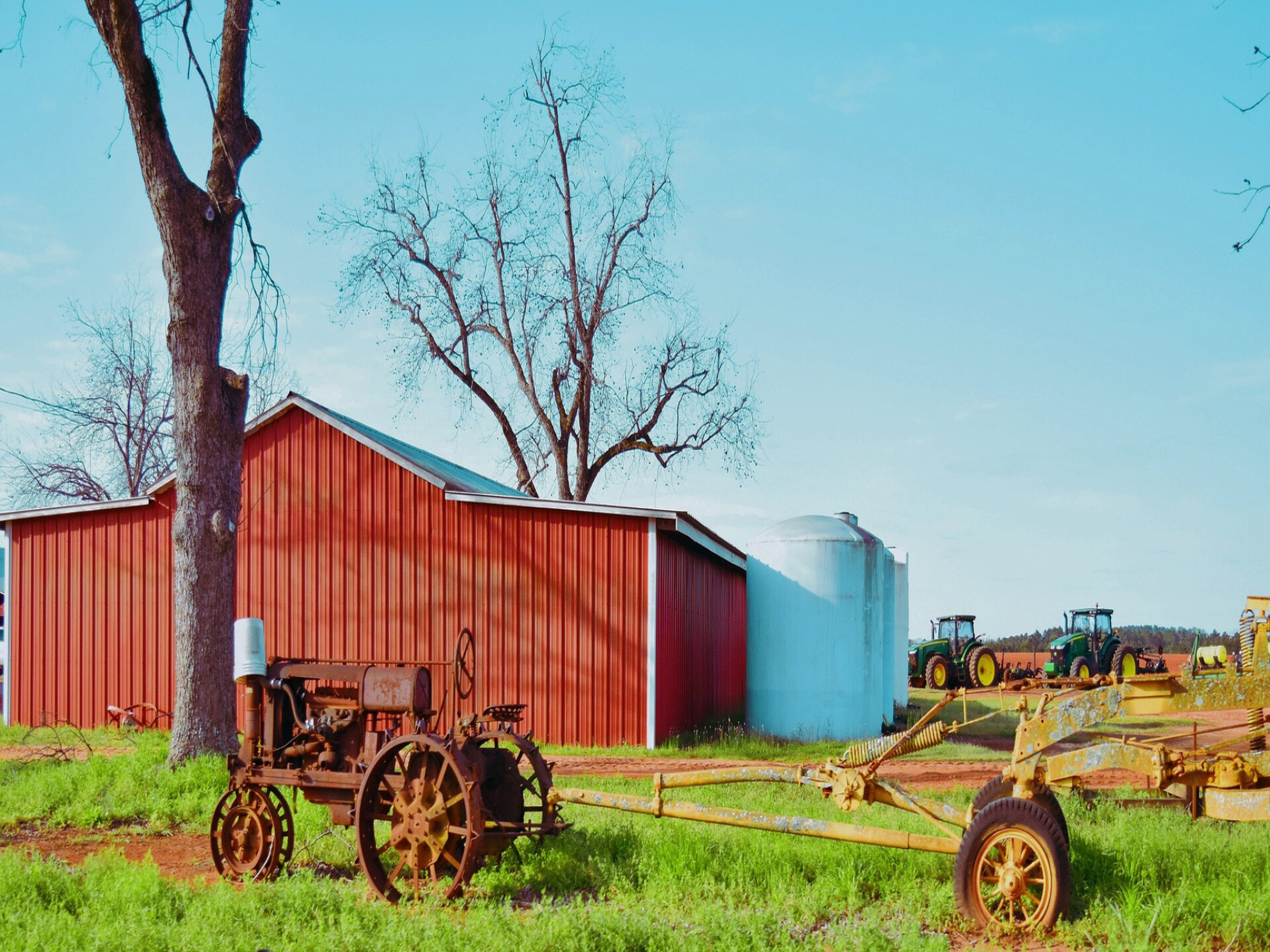 Red barn and silo with vintage farm equipment in a grassy field