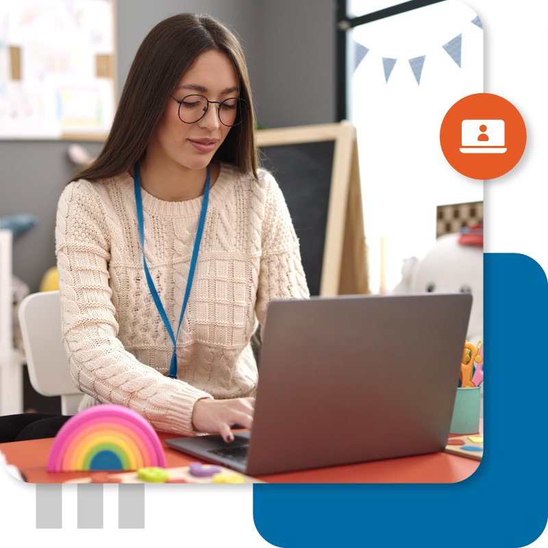 Educator sitting at a desk using a laptop in a classroom.